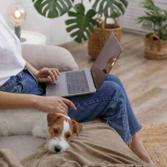 Young woman working on her laptop while her dog rests next to her